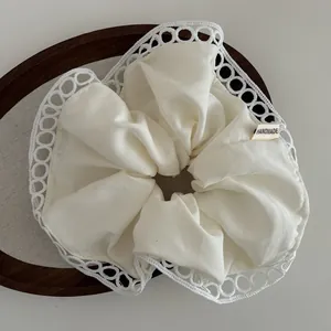 Detail of cream scrunchie with lace trim and handmade label on a wooden tray