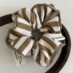 Close-up of brown and white striped knit scrunchie with cute baby label on linen