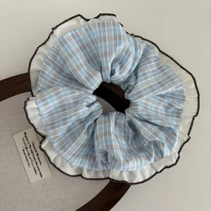 Close-up of blue plaid scrunchie with white ruffles and brown stitching detail