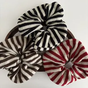 Three striped knitted scrunchies in black, brown, and red on a round wooden tray
