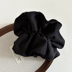 Dettaglio di un grande elastico scrunchie in tessuto nero su vassoio in legno
