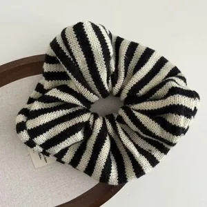 Detail of a knitted oversized scrunchie with black and white stripes on a wooden tray