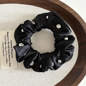 Close-up of black satin scrunchie featuring elegant silver beads and crystal rhinestone details