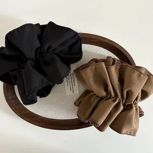 Scrunchies in tessuto plissettato oversize nero e marrone su un vassoio di legno vintage