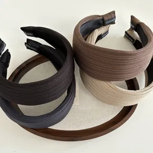 Detail of four wide textured headbands in Morandi tones arranged on a wooden tray