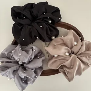 Detail of satin hair scrunchies with white pearls and silver studs in a wooden tray