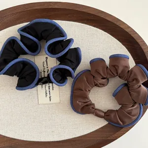 Detailed view of black and brown pleated scrunchies with denim trim on a wooden tray