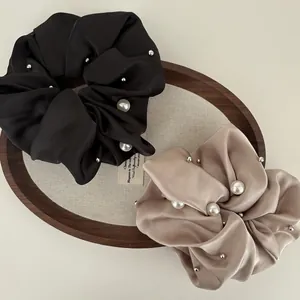 Detailed view of satin scrunchies with white pearls on a minimalist wooden tray