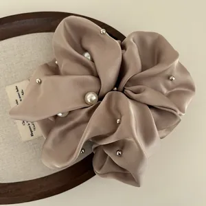Close-up of champagne satin scrunchie with faux pearls and silver rivets detail