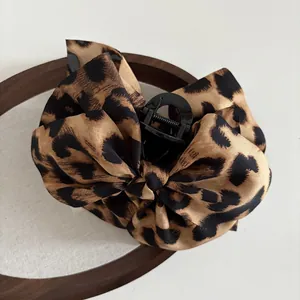 Macro detail of leopard print fabric bow hair claw clip with glossy black teeth