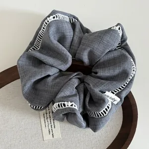 Detailed close-up of grey fabric hair scrunchie with white lace trim on wooden tray