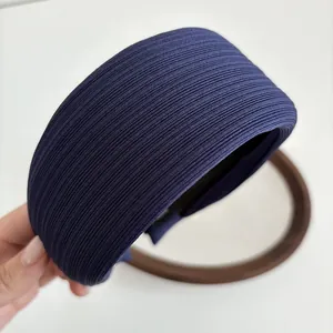 Detail of dark blue wide headband with textured vertical stripes held against a round mirror