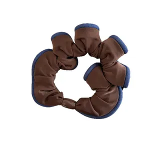 Brown ruffled hair scrunchie with navy blue trim on a minimalist white background