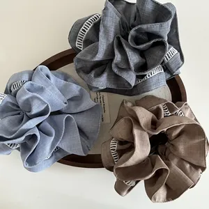 Close-up of three layered fabric scrunchies with white eyelet embroidery in a wooden tray