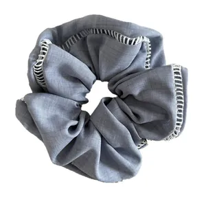 Light blue fabric scrunchie with white eyelet lace trim and pleated texture