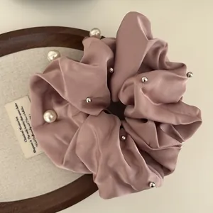 Pink satin scrunchie featuring white pearls and beads on a round wooden tray