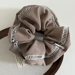 Brown fabric scrunchie with white lace trim and cute baby tag on wooden display base