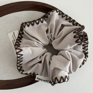 Close-up of light gray scrunchie with dark brown hand-stitched edges and cute baby tag