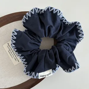 Detail of dark blue scrunchie with white hand-stitched edges and 'cute baby' woven label