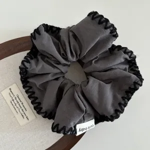 Detail of grey hair scrunchie with black hand-stitched edges and cute baby woven label