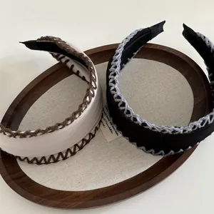 Close-up of wide hand-stitched crochet headbands in beige and black on a tray