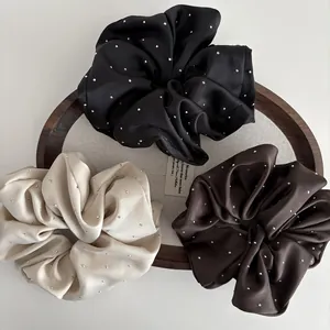 Close-up of three satin scrunchies in black, beige, and brown with sparkling rhinestones