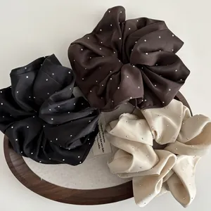 Close-up of three satin scrunchies with silver studs in a wooden tray