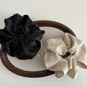 Close-up of black and champagne satin scrunchies with rhinestones on a wooden tray