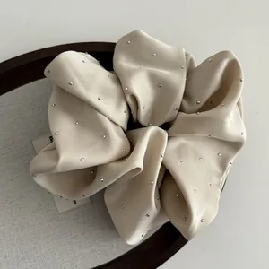 Close-up of elegant beige satin scrunchie featuring delicate silver rhinestones