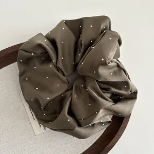 Close-up of olive green satin scrunchie with sparkling rhinestones on display