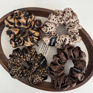 Close-up of four assorted leopard print fabric scrunchies with Hand Made woven labels