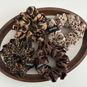 Detail of four leopard print scrunchies with Hand Made labels on a wooden tray