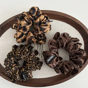 Detailed set of three leopard print fabric scrunchies with handmade labels on a tray