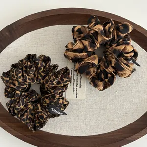 Detailed close-up of leopard print hair scrunchies with 'Hand Made' woven label on wooden tray
