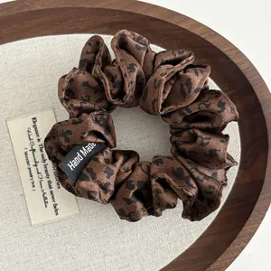 Macro detail of leopard print satin scrunchie with Hand Made label on wooden tray