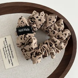 Detail of leopard print fabric scrunchie with a Hand Made label in a wooden tray