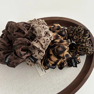 Set of four leopard print satin hair scrunchies with handmade labels on wooden tray