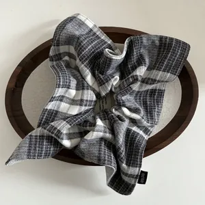 Close-up of a classic grey plaid scrunchie with a Hand Made tag in a wooden tray