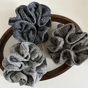 Close-up of three knitted oversized scrunchies in mixed grey tones on a wooden tray