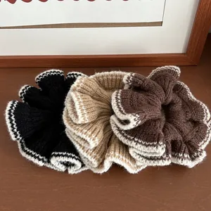 Détail de trois chouchous en tricot noir, beige et café avec bordure ondulée contrastée