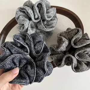 Detail view of oversized knitted scrunchies in three shades of grey on a wooden tray