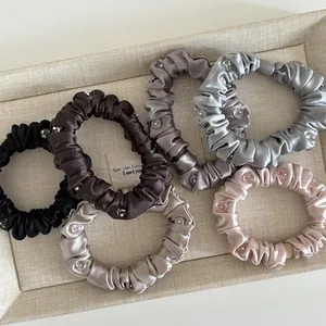 Close-up of six satin scrunchies with crystal rhinestones on a beige linen display tray