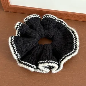 Détail d'un chouchou en tricot noir avec bordure ondulée blanche sur fond en bois