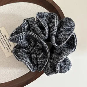 Detail of dark grey and white knit scrunchie with soft wool texture on wooden tray