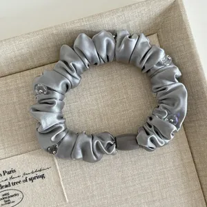 Close-up of a grey satin scrunchie featuring elegant crystal bead accents on a display tray
