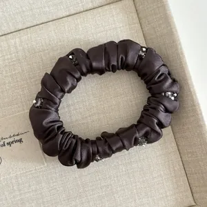 Detail of dark brown satin scrunchie with crystal beads on soft textured fabric