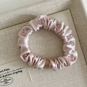 Close-up of pale pink satin hair scrunchie with transparent pink crystal beads and fine pleats