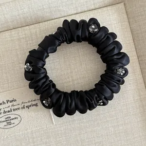 Detail of black satin scrunchie with pleated texture and grey crystal embellishments