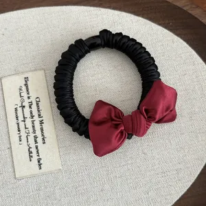 Close-up of deep red satin bow and pleated black elastic hair tie on a wooden table