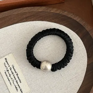 Close-up of black satin pleated scrunchie with a large pearl bead on a wooden tray